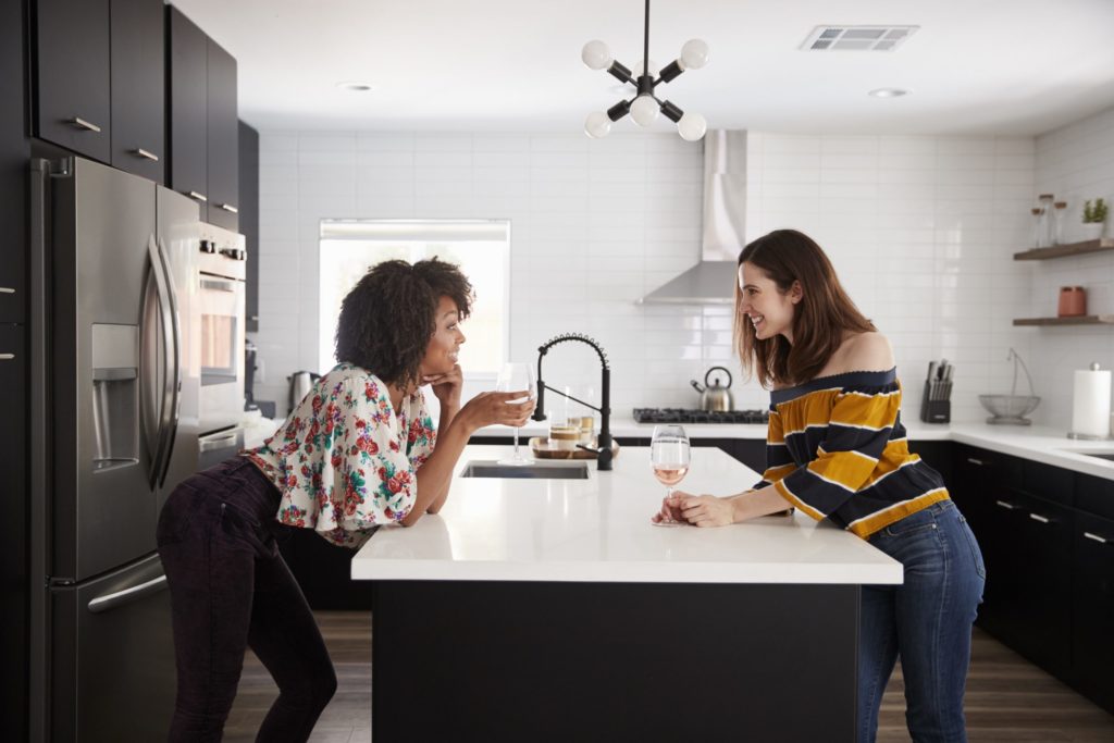 Two women chatting and having wine around an industrial-style kitchen island that is heated with FeelsWarm heating mats.