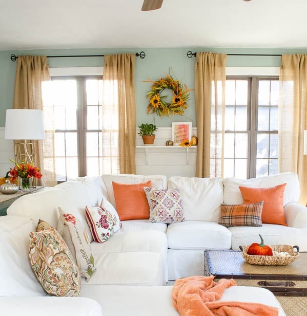 A living room with a white sectional couch with orange pillows.