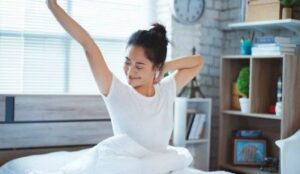 woman in white T shirt stretching arms after waking up